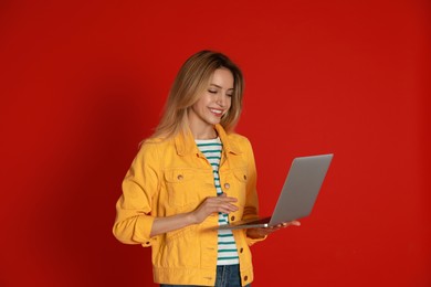 Photo of Young woman with modern laptop on red background