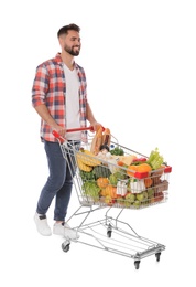 Photo of Happy man with shopping cart full of groceries on white background