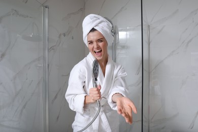 Photo of Beautiful young woman singing into showerhead in bathroom