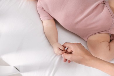 Mother holding hand of her baby on bed, top view