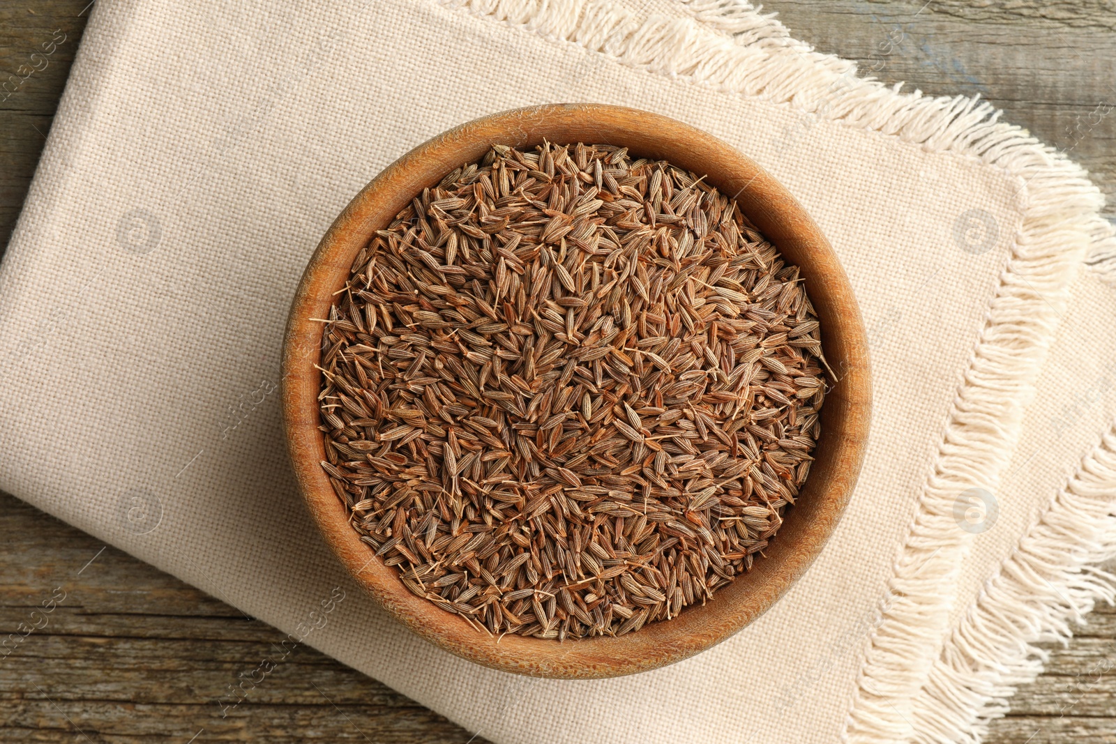 Photo of Bowl of caraway seeds and napkin on wooden table, top view