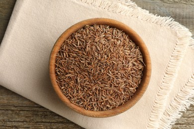 Photo of Bowl of caraway seeds and napkin on wooden table, top view