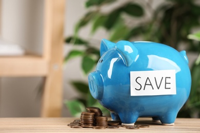 Photo of Piggy bank with word SAVE and coins on wooden table against blurred background