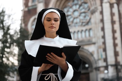 Photo of Young nun reading Bible near cathedral outdoors