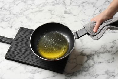 Photo of Woman holding frying pan with melting butter on marble background, closeup