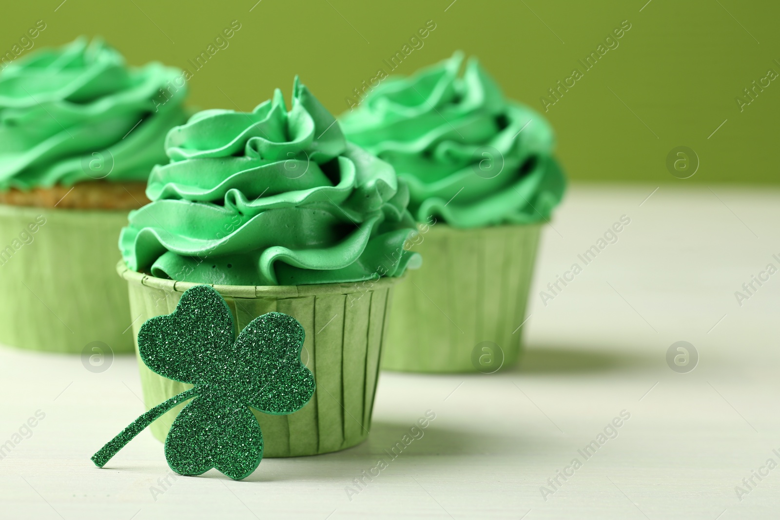 Photo of St. Patrick's day party. Tasty cupcakes with green cream on white table, closeup. Space for text