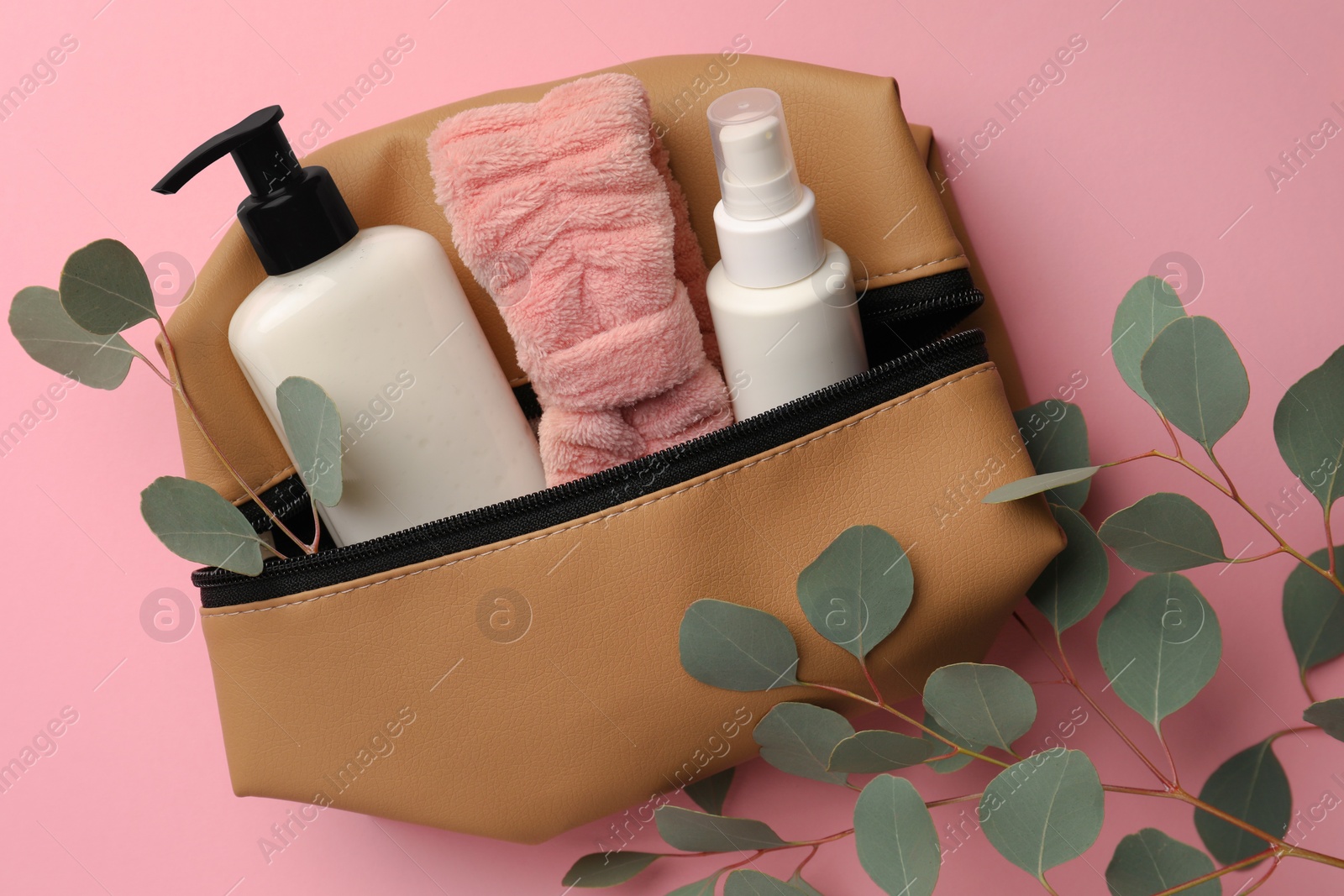 Photo of Preparation for spa. Compact toiletry bag with different cosmetic products and eucalyptus on pink background, flat lay