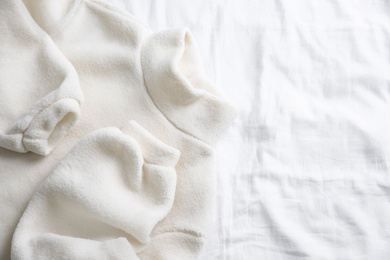 Photo of Warm fleece sweater on white crumpled fabric, top view. Space for text