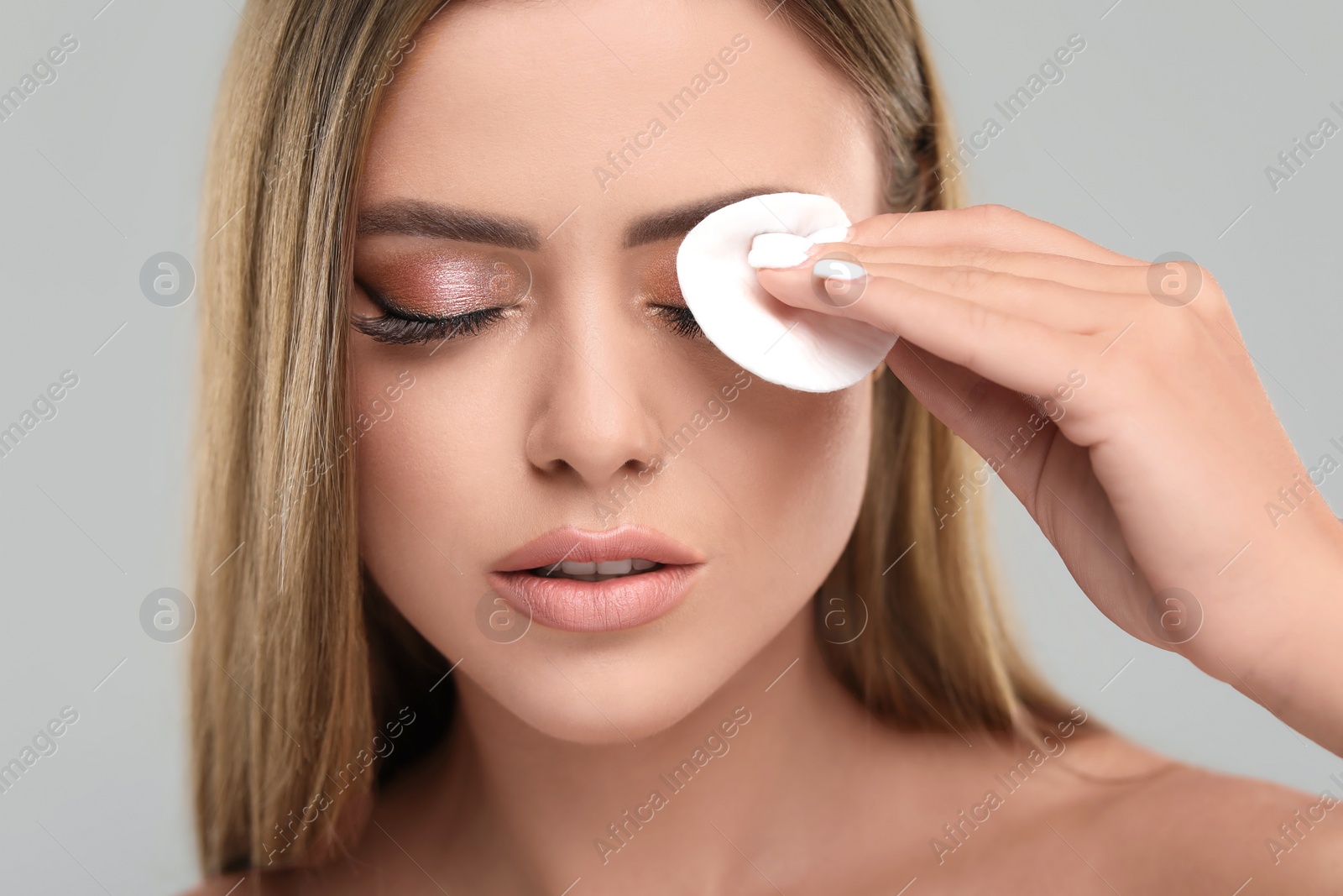 Photo of Beautiful woman removing makeup with cotton pad on grey background, closeup