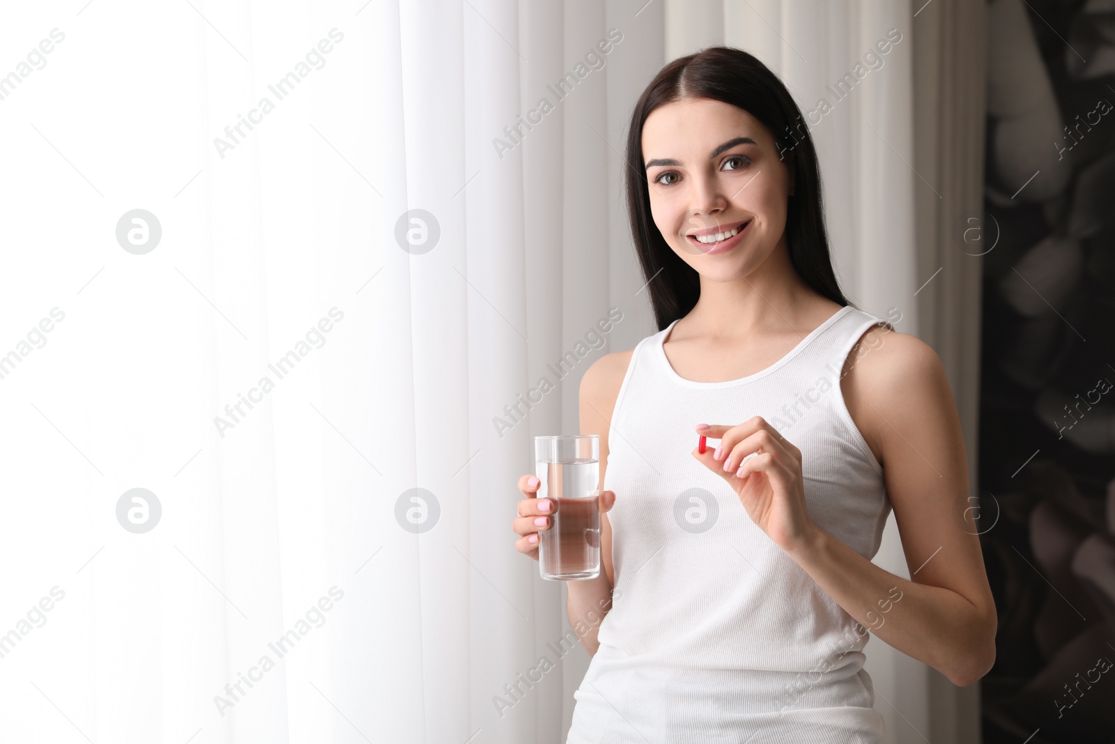 Photo of Woman with glass of water and vitamin capsule indoors. Space for text