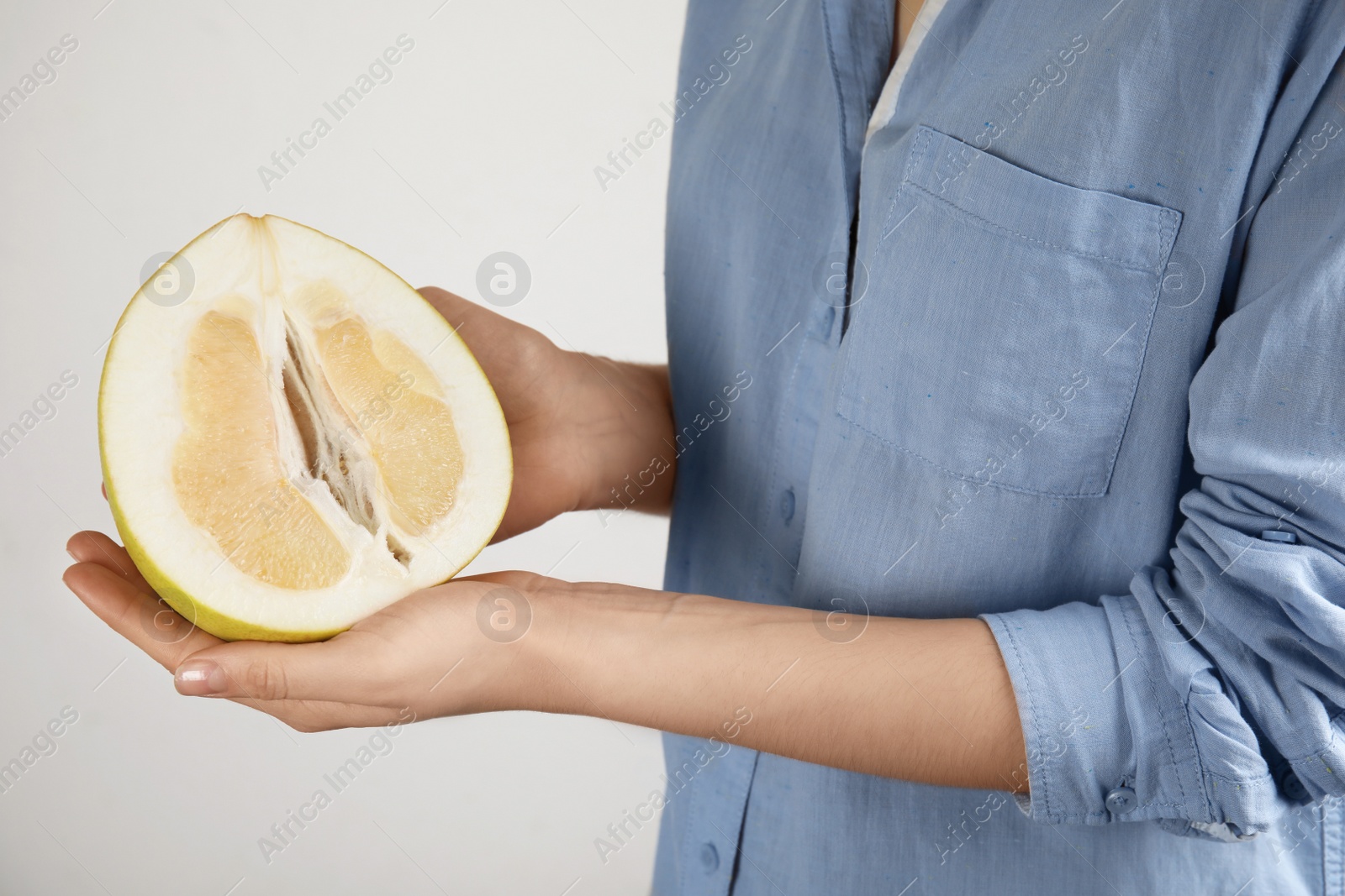 Photo of Woman holding half of fresh ripe pomelo on light background, closeup