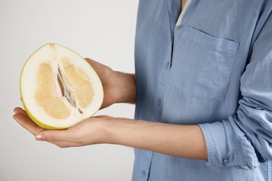 Photo of Woman holding half of fresh ripe pomelo on light background, closeup