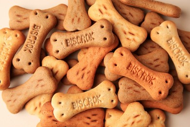 Photo of Pile of bone shaped dog cookies on beige background, flat lay