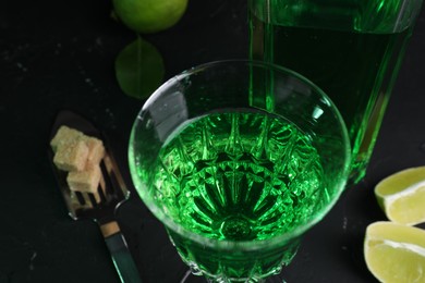 Absinthe in glass, spoon, brown sugar and lime on black table, closeup. Alcoholic drink