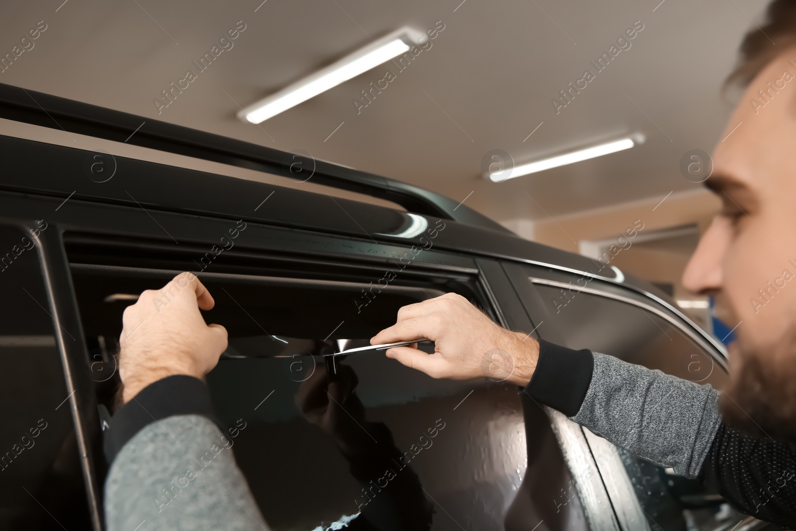 Photo of Worker tinting car window in shop, closeup