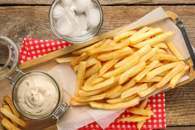 Delicious french fries served with sauce and glass of water on wooden table, flat lay