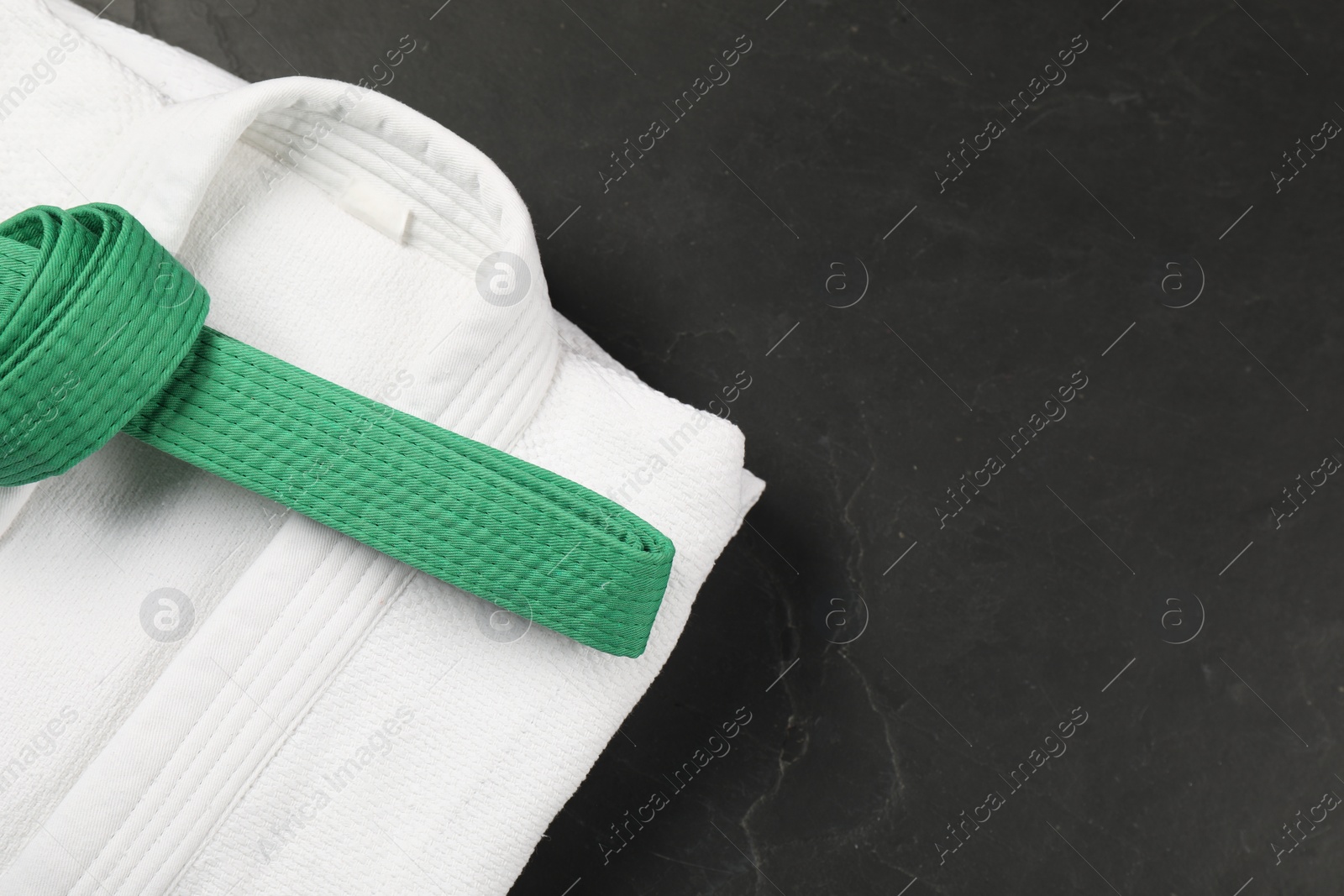 Photo of Green karate belt and white kimono on gray background, top view. Space for text