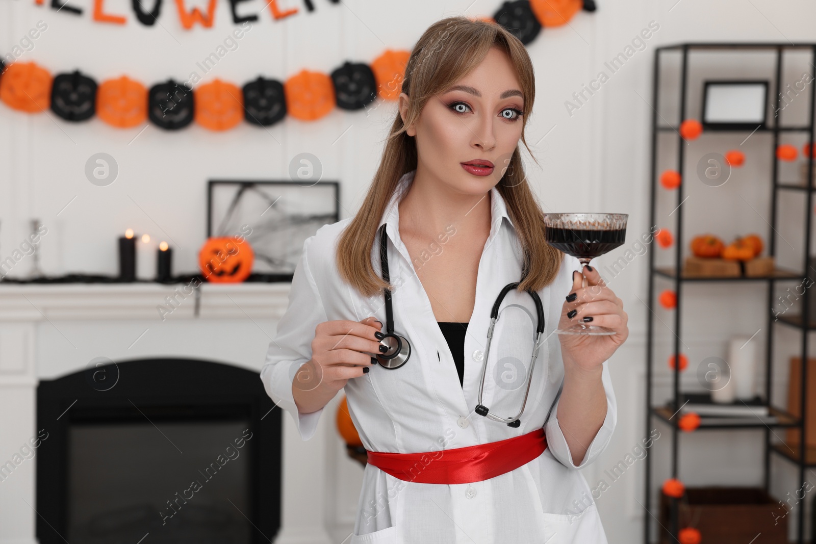 Photo of Woman in scary nurse costume with glass of wine indoors. Halloween celebration