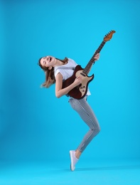 Young woman playing electric guitar on color background