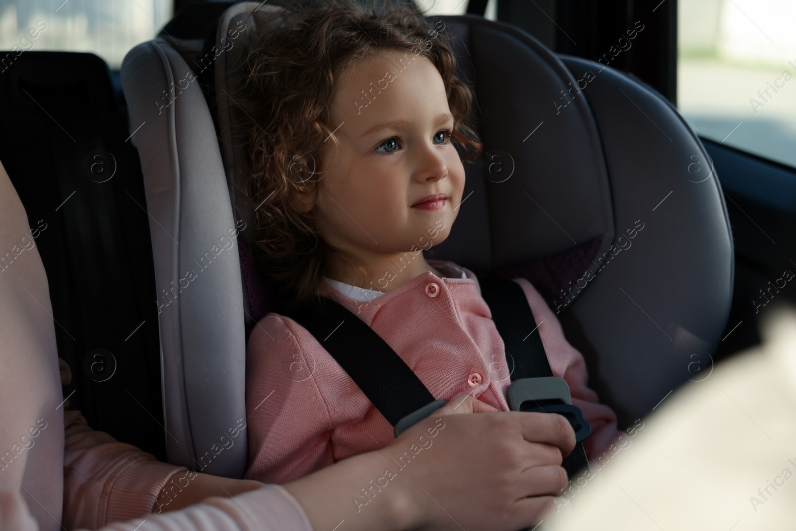 Photo of Mother fastening her daughter in child safety seat inside car