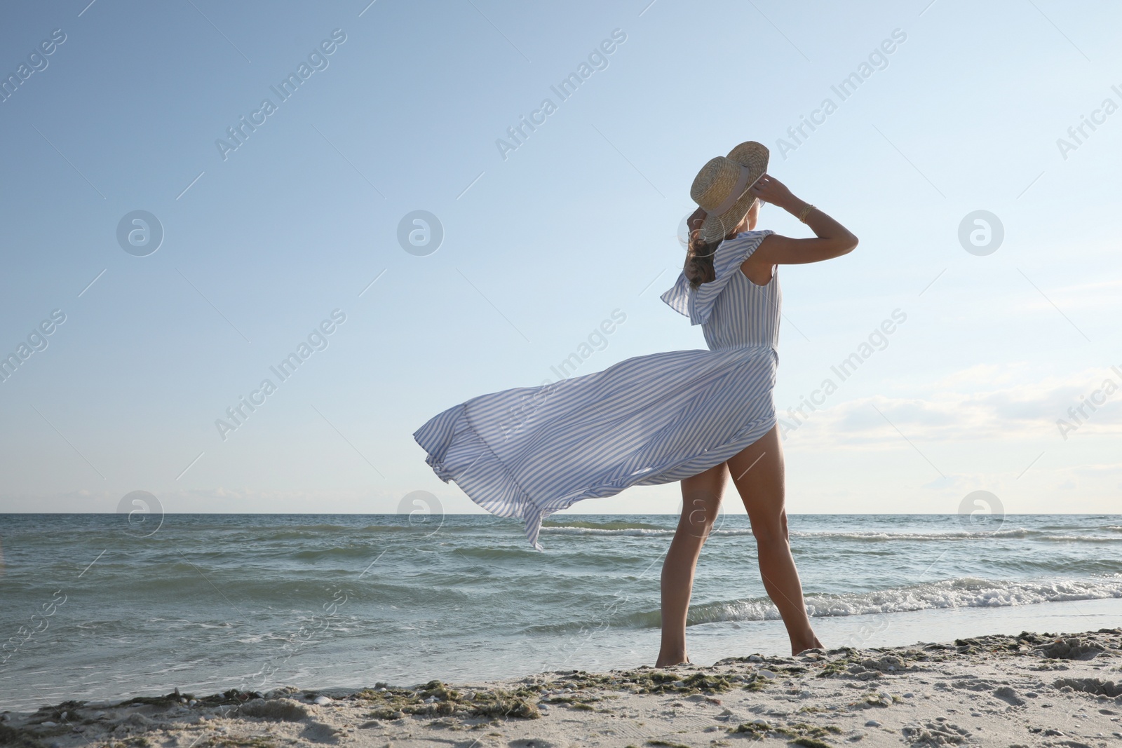 Photo of Woman in dress with straw hat walking by sea on sunny day