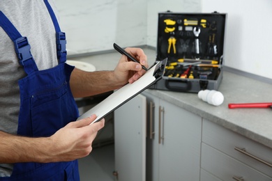 Photo of Male plumber writing in clipboard indoors, closeup with space for text. Repair service