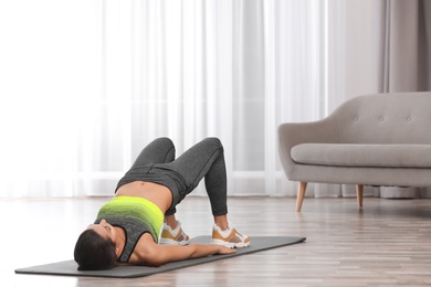 Young woman in fitness clothes doing exercise at home. Space for text