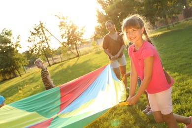 Group of children and teacher playing with rainbow playground parachute on green grass. Summer camp activity