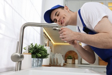 Photo of Smiling plumber repairing faucet with spanner in kitchen, low angle view