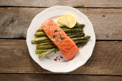 Photo of Tasty grilled salmon with asparagus and lemon on wooden table, top view