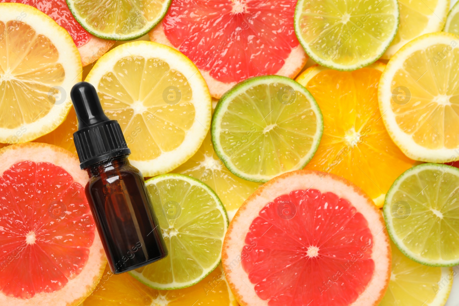 Photo of Bottle of essential oil on pile of citrus slices, flat lay. Space for text