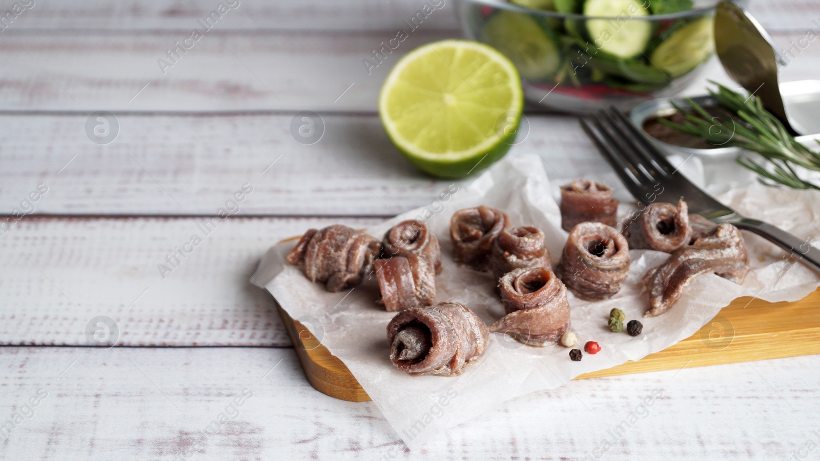 Photo of Canned anchovy fillets, rosemary and lime on white wooden table, space for text