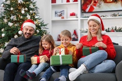 Photo of Happy family in Santa hats with Christmas gifts on sofa at home