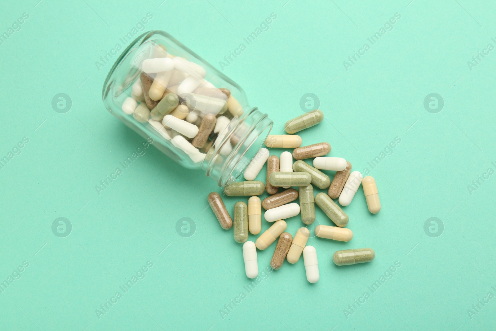 Photo of Vitamin pills and bottle on mint color background, top view