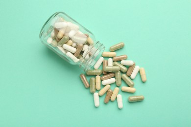 Photo of Vitamin pills and bottle on mint color background, top view