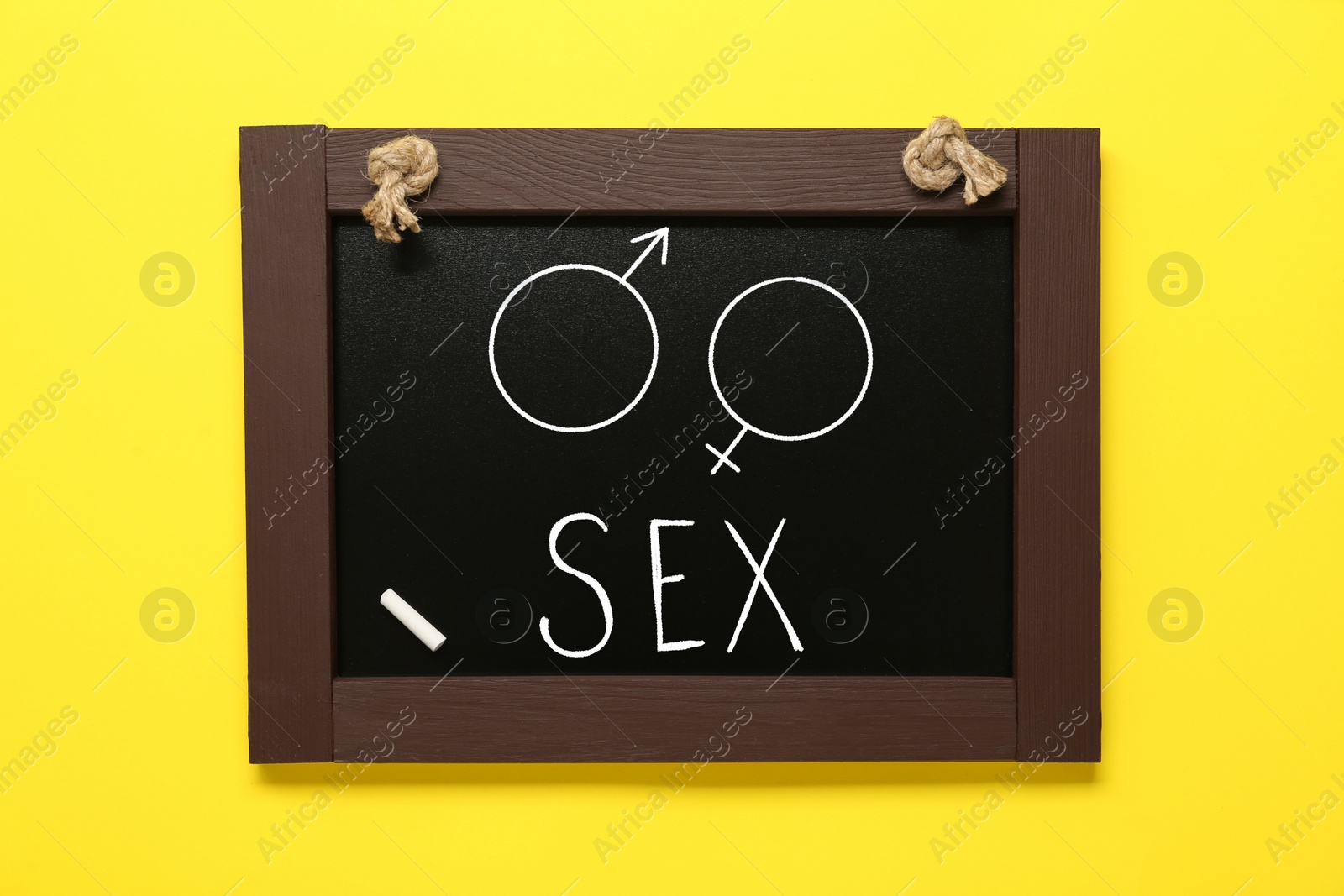 Image of Sexual education. Small black chalkboard with word Sex, female and male gender signs on yellow background, top view