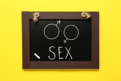 Sexual education. Small black chalkboard with word Sex, female and male gender signs on yellow background, top view