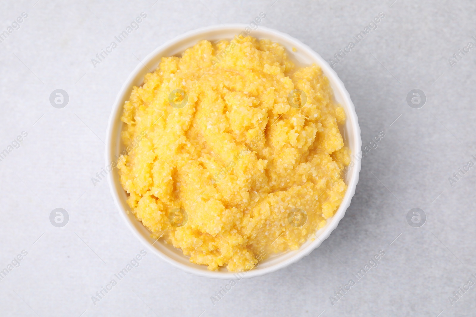 Photo of Tasty cornmeal in bowl on light gray table, top view