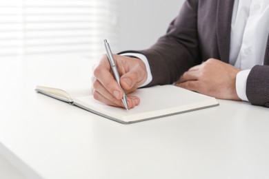 Photo of Man writing in notebook at white table indoors, closeup