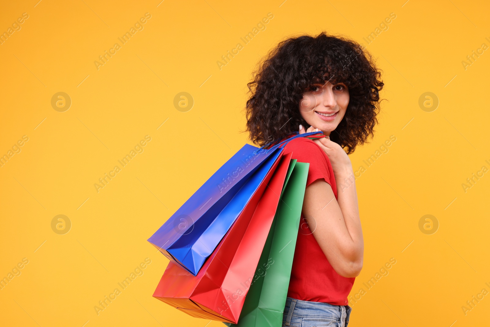 Photo of Happy young woman with shopping bags on yellow background