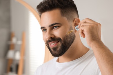 Photo of Handsome man applying cosmetic serum onto his face in bathroom