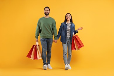 Happy couple with shopping bags on orange background