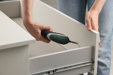 Photo of Woman with electric screwdriver assembling drawer, closeup