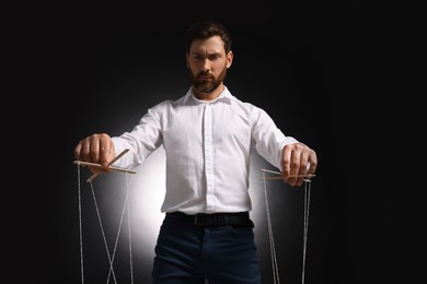 Photo of Man in formal outfit pulling strings of puppet on dark background, low angle view