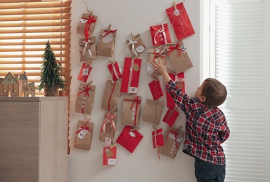 Cute little boy taking gift from Advent calendar at home, back view. Christmas tradition