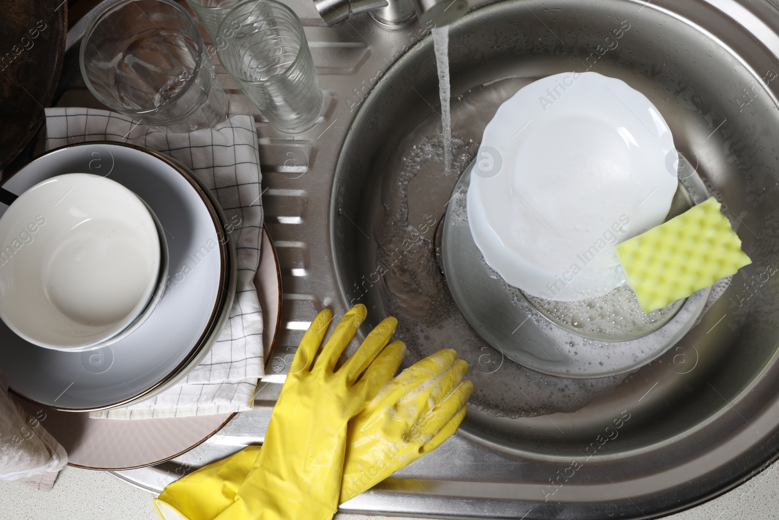 Photo of Washing plates, sponge and rubber gloves in kitchen sink, above view