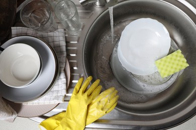 Photo of Washing plates, sponge and rubber gloves in kitchen sink, above view