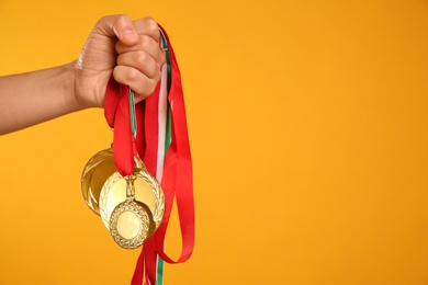 Photo of Woman holding gold medals on yellow background, closeup. Space for text