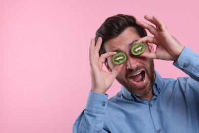 Photo of Emotional man holding halves of kiwi near his eyes on pink background, space for text