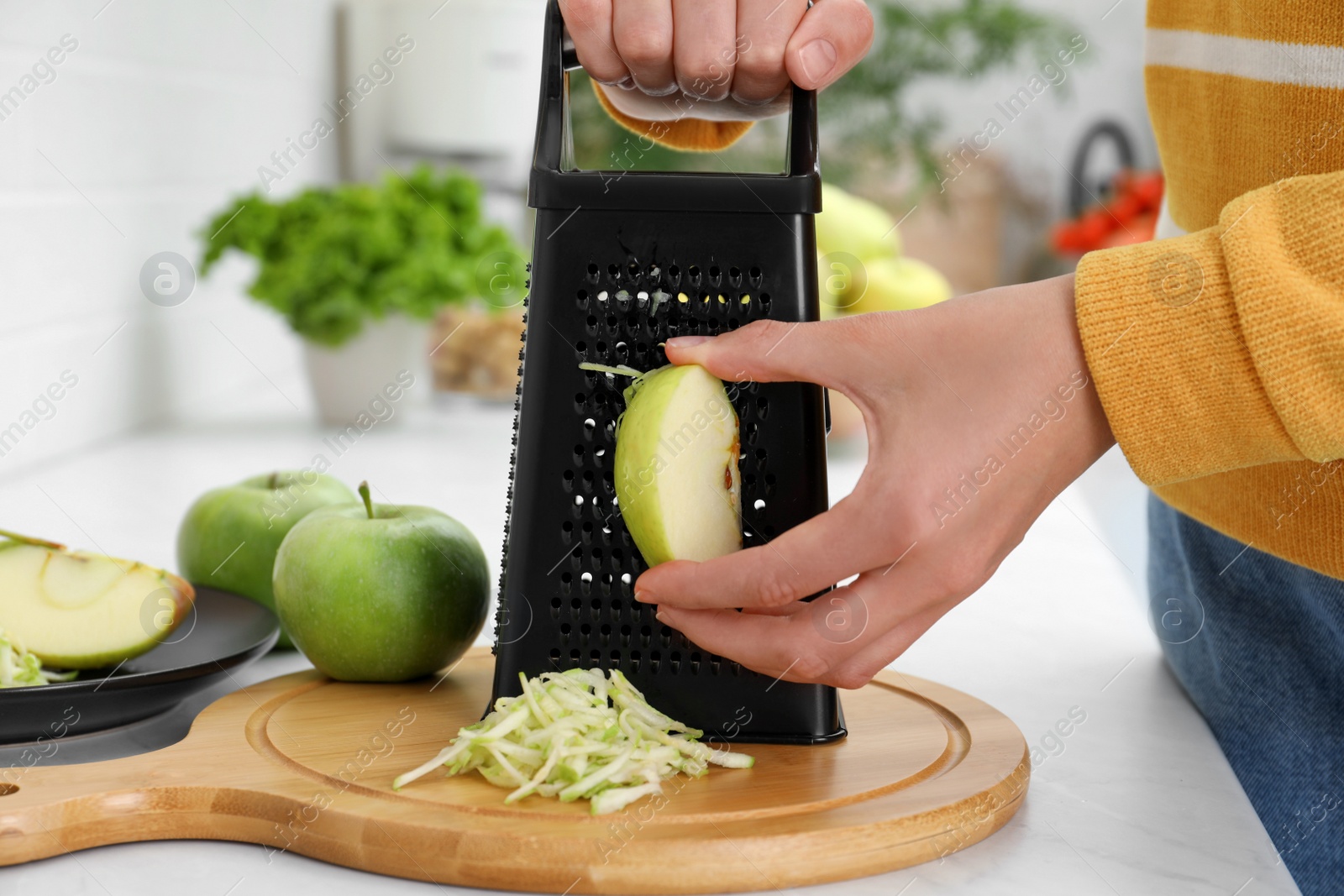 Photo of Woman grating fresh green apple at kitchen counter, closeup